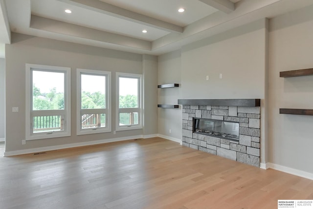 unfurnished living room with beam ceiling, light wood-type flooring, a fireplace, and a wealth of natural light