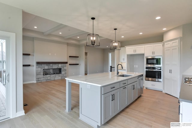 kitchen with a center island with sink, stainless steel appliances, light stone counters, sink, and white cabinetry