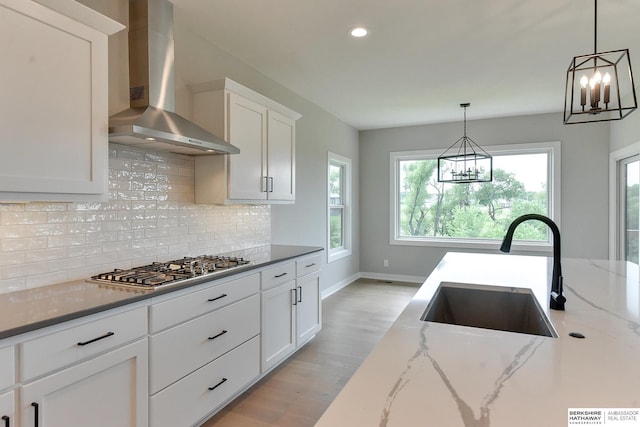 kitchen featuring hanging light fixtures, sink, white cabinets, dark stone counters, and wall chimney range hood