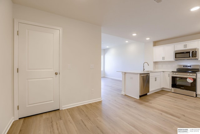 kitchen featuring a peninsula, a sink, stainless steel appliances, light wood-style floors, and white cabinetry