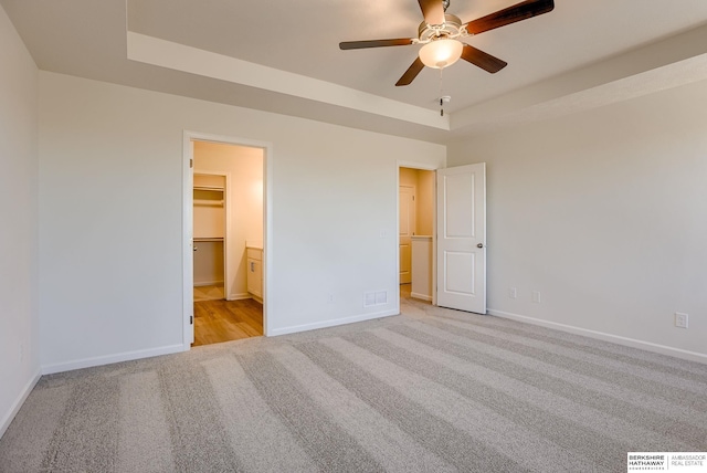 unfurnished bedroom featuring visible vents, a walk in closet, baseboards, light carpet, and a raised ceiling