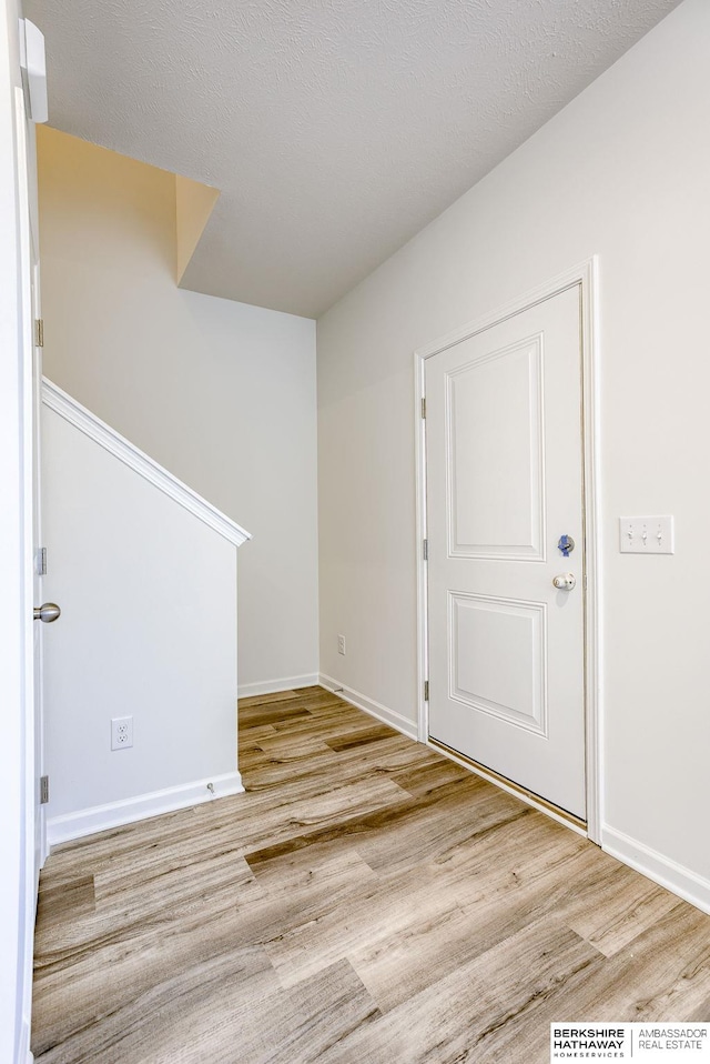 foyer entrance featuring a textured ceiling, baseboards, and wood finished floors