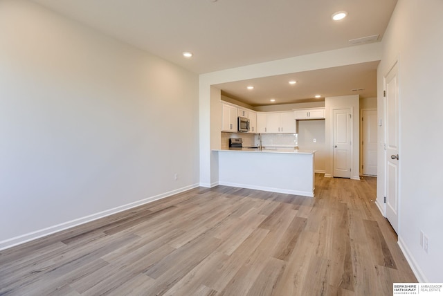 kitchen featuring light wood-style flooring, stainless steel appliances, a peninsula, white cabinets, and baseboards