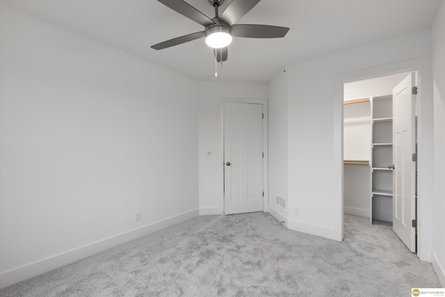 unfurnished bedroom featuring ceiling fan, a spacious closet, light carpet, and a closet