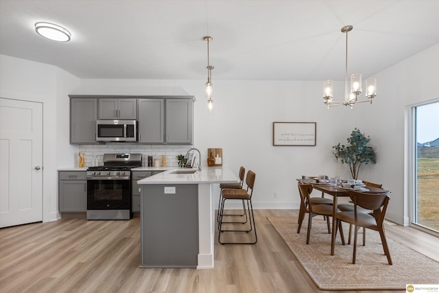 kitchen with kitchen peninsula, backsplash, gray cabinetry, stainless steel appliances, and pendant lighting