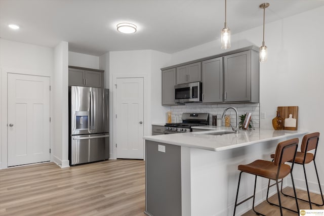 kitchen featuring gray cabinetry, stainless steel appliances, tasteful backsplash, kitchen peninsula, and decorative light fixtures