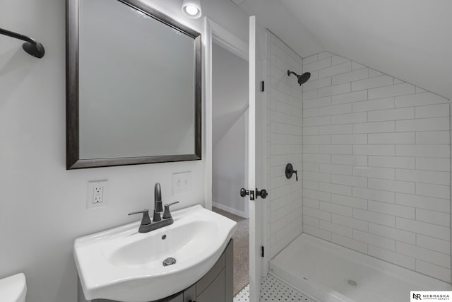 bathroom with tiled shower, sink, and vaulted ceiling