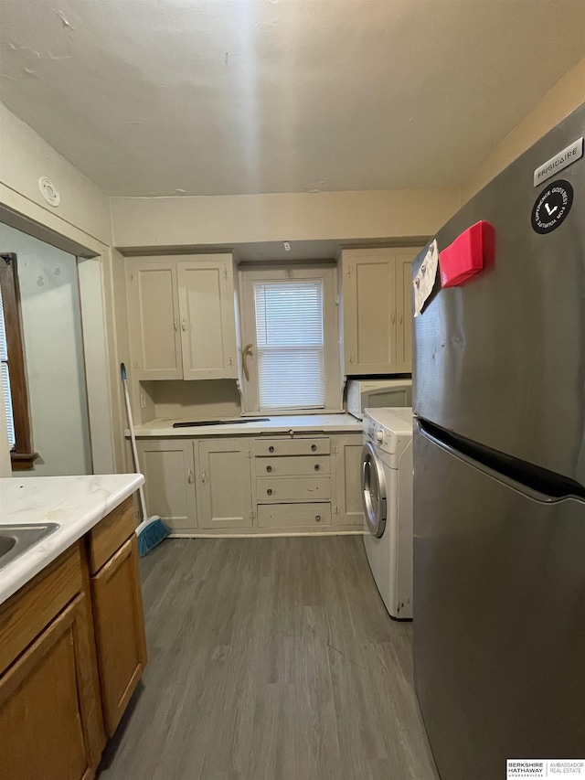 kitchen featuring stovetop, washer / dryer, light wood-type flooring, and stainless steel refrigerator