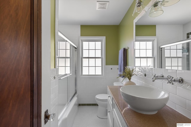 full bathroom with tile patterned flooring, tile walls, toilet, bath / shower combo with glass door, and vanity