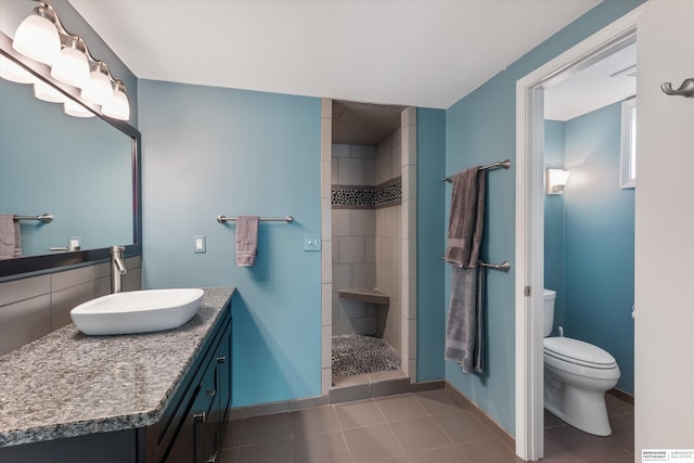 bathroom with tile patterned flooring, a tile shower, vanity, and toilet