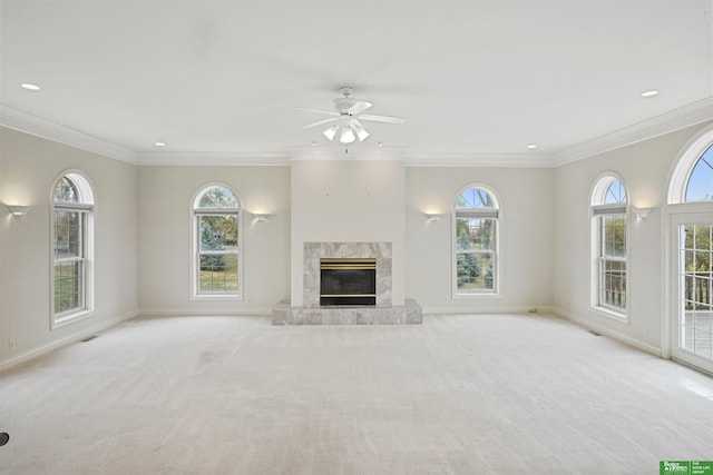 unfurnished living room featuring plenty of natural light, ceiling fan, light colored carpet, and a high end fireplace