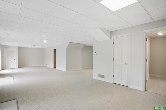 basement with a paneled ceiling and light colored carpet