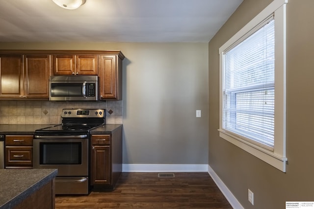 kitchen with appliances with stainless steel finishes, dark hardwood / wood-style floors, tasteful backsplash, and plenty of natural light