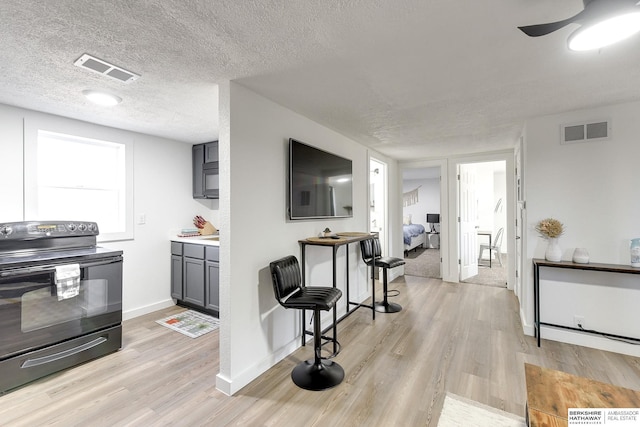 kitchen featuring a textured ceiling, ceiling fan, light hardwood / wood-style flooring, gray cabinets, and black / electric stove