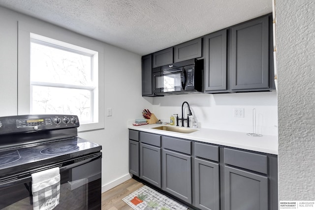 kitchen featuring sink, a textured ceiling, light wood-type flooring, black appliances, and gray cabinetry