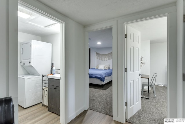 corridor with stacked washer and clothes dryer and light hardwood / wood-style floors