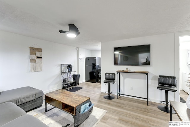 living room featuring light wood-type flooring, ceiling fan, and a textured ceiling