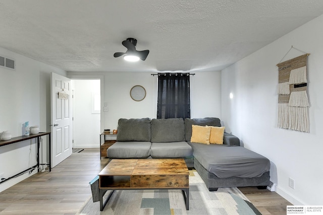 living room with a textured ceiling, ceiling fan, and hardwood / wood-style flooring