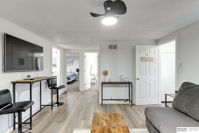 living room featuring a textured ceiling, ceiling fan, and light wood-type flooring