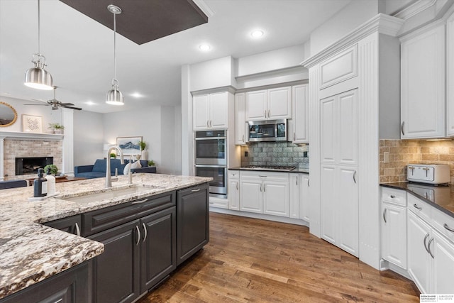 kitchen with stainless steel appliances, a brick fireplace, tasteful backsplash, and dark stone counters