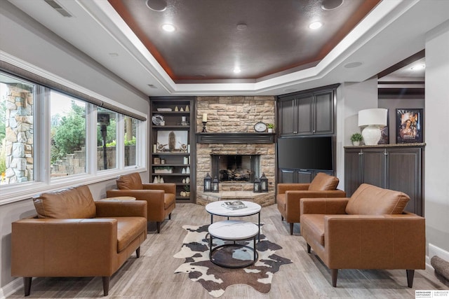 living room with a raised ceiling, built in shelves, a fireplace, and light wood-type flooring