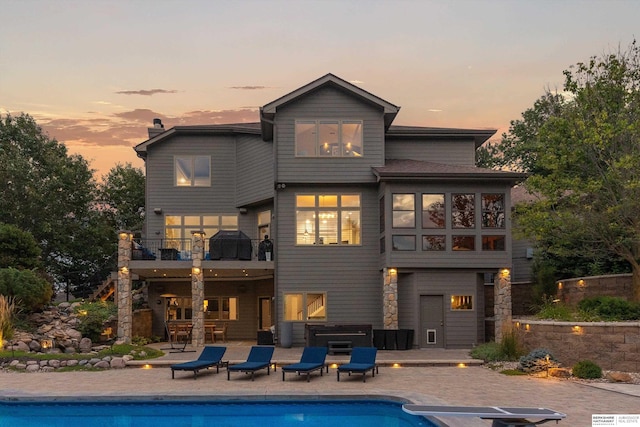 back house at dusk featuring a balcony and a patio area