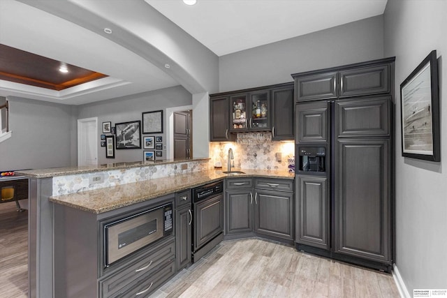 kitchen featuring light stone countertops, kitchen peninsula, black microwave, and tasteful backsplash