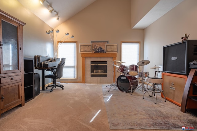 home office with a tiled fireplace, carpet, track lighting, and high vaulted ceiling