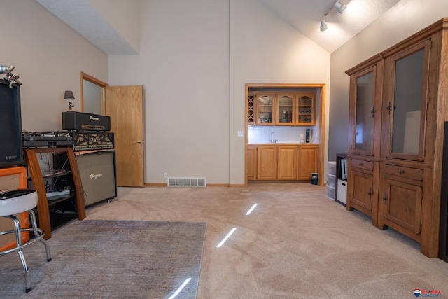 kitchen featuring decorative backsplash, track lighting, light colored carpet, sink, and high vaulted ceiling