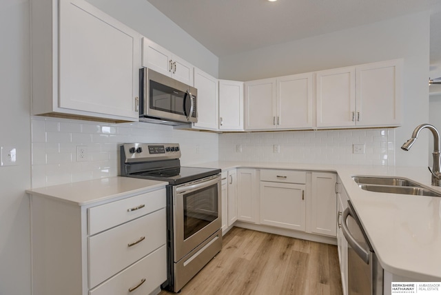 kitchen featuring decorative backsplash, stainless steel appliances, sink, white cabinets, and light hardwood / wood-style floors