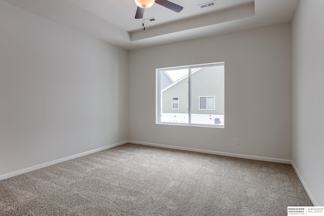 empty room with a tray ceiling, ceiling fan, and carpet flooring