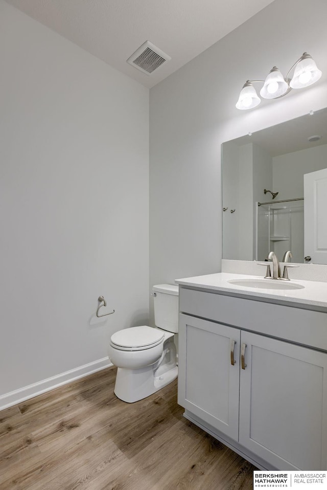 bathroom featuring a shower with door, vanity, hardwood / wood-style floors, and toilet