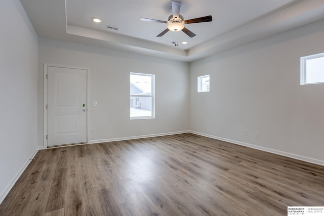 empty room featuring a tray ceiling, ceiling fan, and wood-type flooring