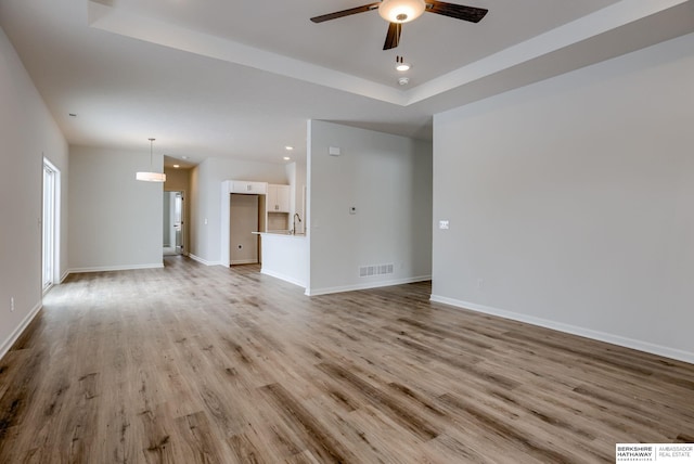 unfurnished living room featuring light hardwood / wood-style flooring, a raised ceiling, ceiling fan, and sink