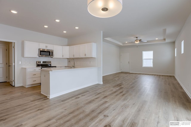 kitchen featuring appliances with stainless steel finishes, a tray ceiling, white cabinetry, and light hardwood / wood-style floors