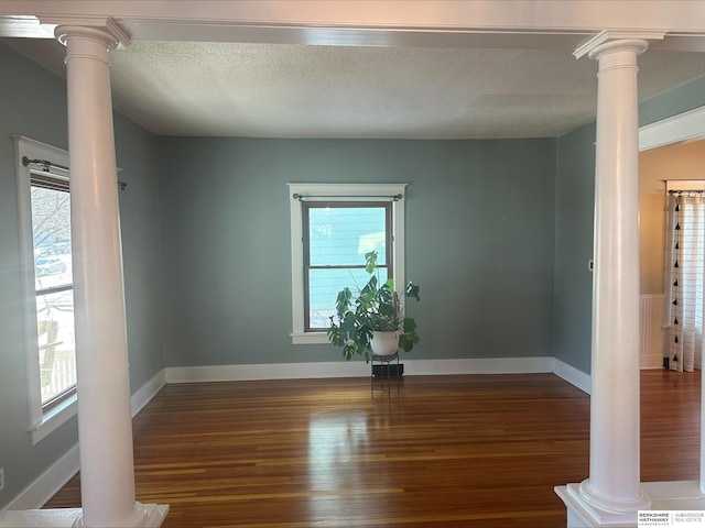 unfurnished room featuring dark hardwood / wood-style flooring, ornate columns, and plenty of natural light