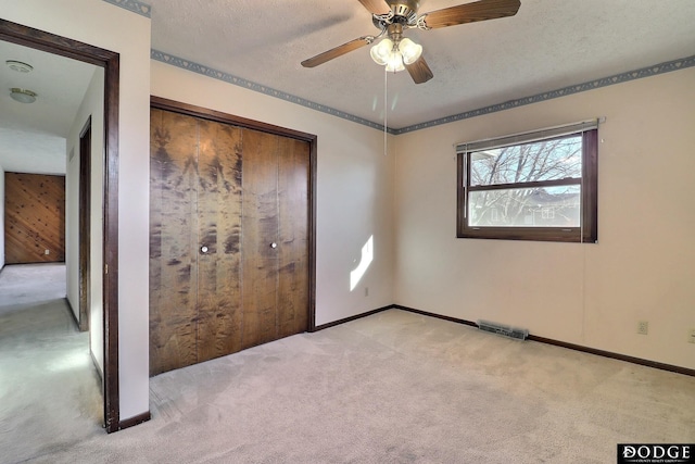 unfurnished bedroom featuring light carpet, a textured ceiling, a closet, and ceiling fan