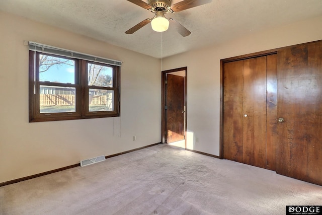 unfurnished bedroom with ceiling fan, light colored carpet, a textured ceiling, and a closet