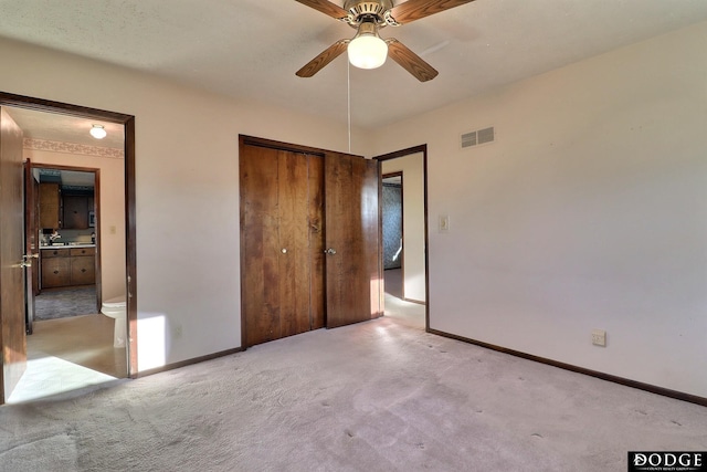 unfurnished bedroom with ensuite bathroom, light colored carpet, a closet, and ceiling fan