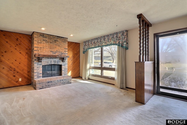 unfurnished living room featuring a fireplace, a textured ceiling, light colored carpet, and wooden walls