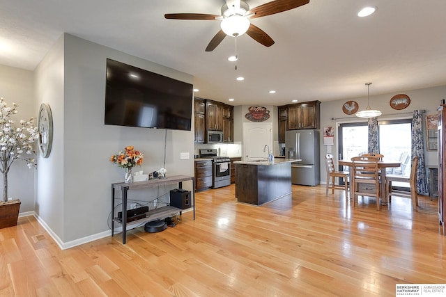 kitchen with appliances with stainless steel finishes, dark brown cabinetry, a kitchen island with sink, sink, and pendant lighting