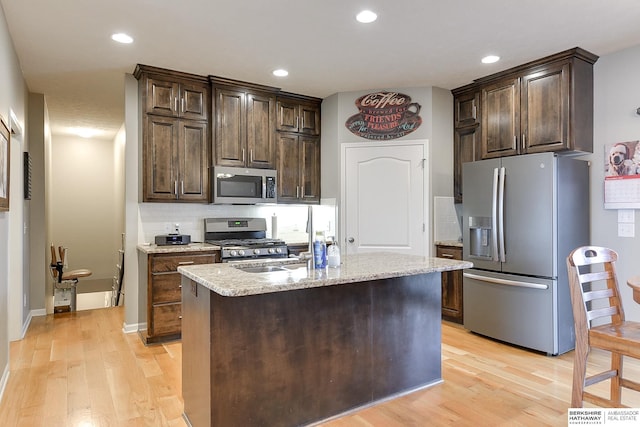 kitchen with appliances with stainless steel finishes, dark brown cabinets, light hardwood / wood-style flooring, and a kitchen island with sink