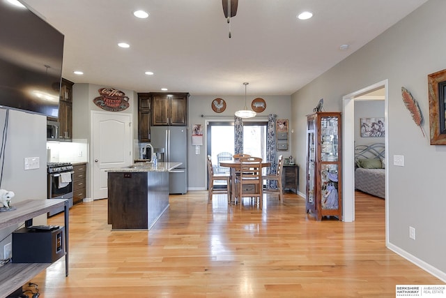 kitchen featuring dark brown cabinetry, light stone counters, an island with sink, pendant lighting, and appliances with stainless steel finishes