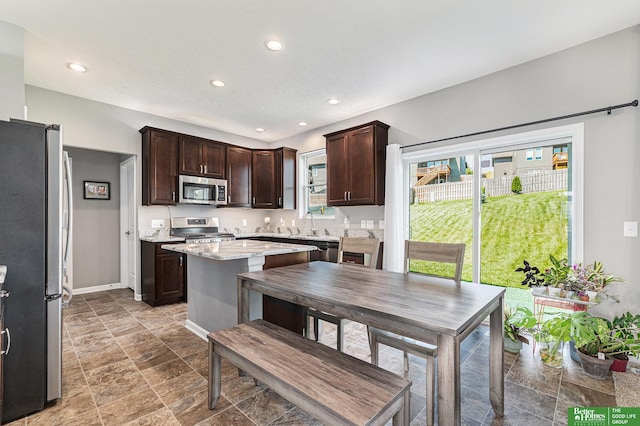 kitchen featuring light stone countertops, appliances with stainless steel finishes, a kitchen island, and dark brown cabinets