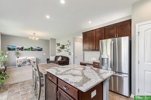 kitchen featuring light stone counters, dark brown cabinetry, a chandelier, stainless steel fridge with ice dispenser, and a kitchen island