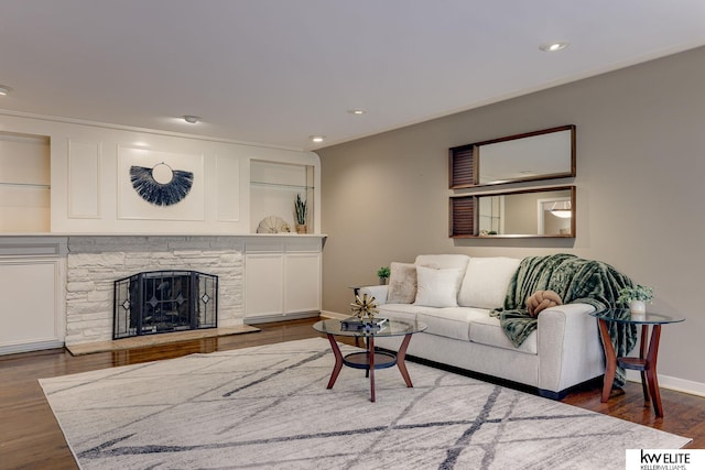 living room with dark hardwood / wood-style floors, a stone fireplace, and built in shelves