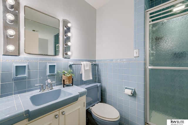 bathroom featuring vanity, toilet, a shower with door, and tile walls