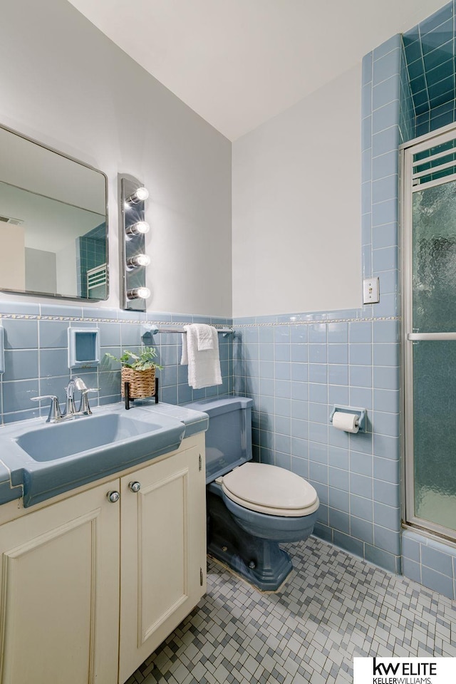 bathroom featuring vanity, a shower with door, tile walls, tile patterned flooring, and toilet