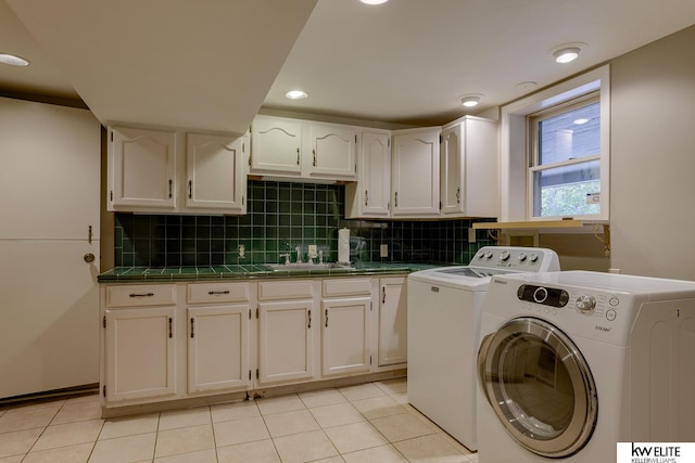 clothes washing area featuring washer and clothes dryer, sink, light tile patterned floors, and cabinets