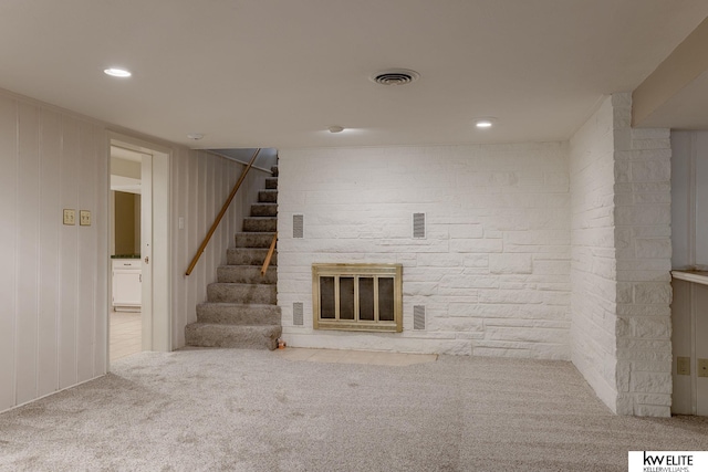 unfurnished living room with carpet flooring, a stone fireplace, and wood walls